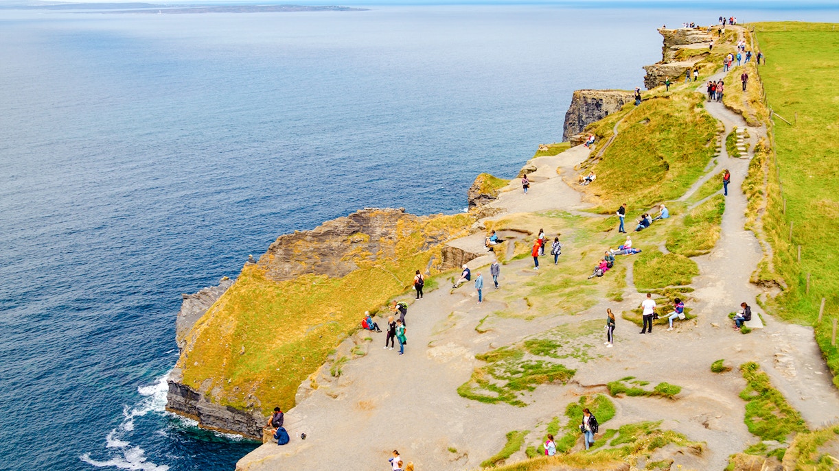 Visitors walking along the Cliffs of Moher, Ireland, with ocean views.