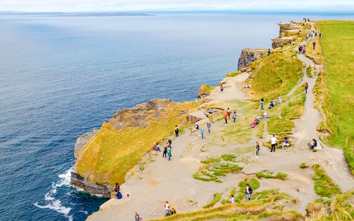 Visitors walking along the Cliffs of Moher, Ireland, with ocean views.