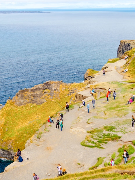 Visitors walking along the Cliffs of Moher, Ireland, with ocean views.