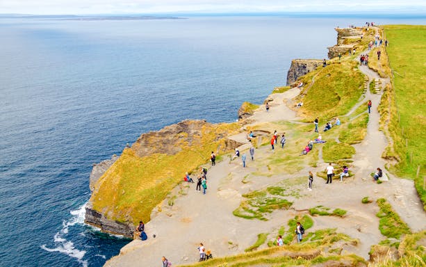 Visitors walking along the Cliffs of Moher, Ireland, with ocean views.