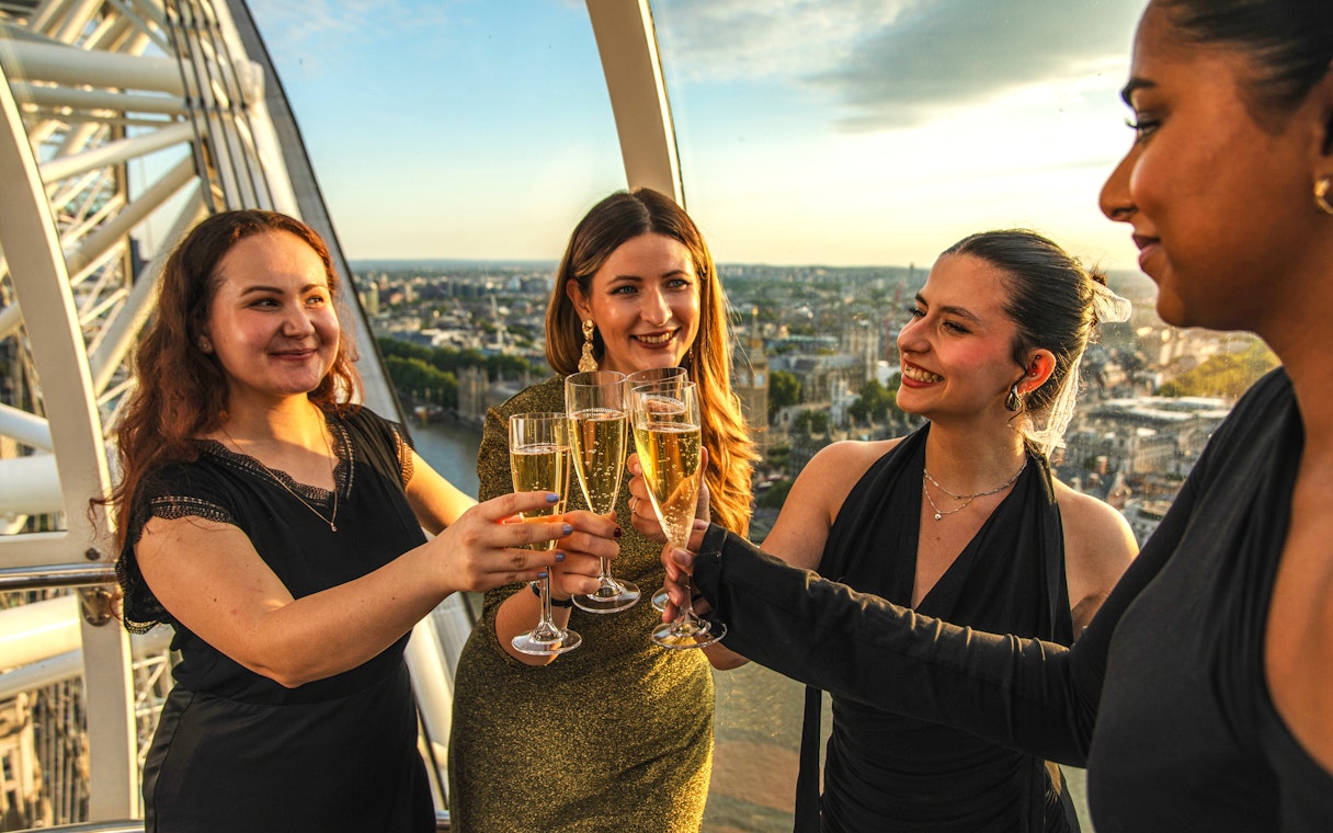 Group toasting with champagne inside London Eye capsule during sunset.