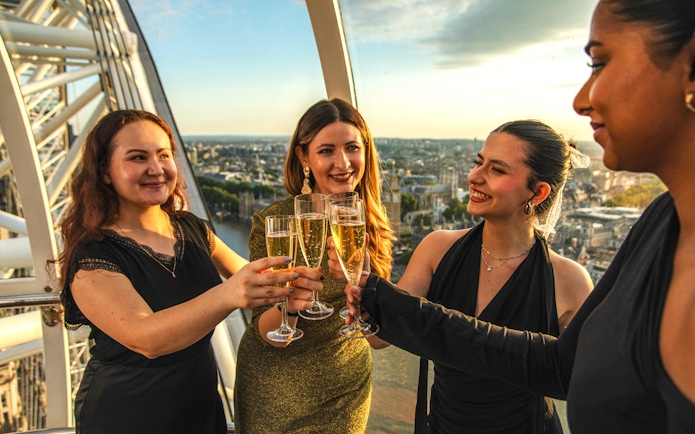Group toasting with champagne inside London Eye capsule during sunset.