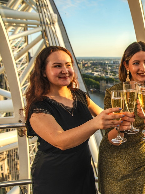 Group toasting with champagne inside London Eye capsule during sunset.