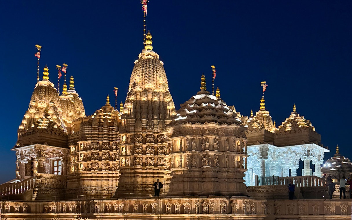 BAPS Hindu Temple illuminated at night, intricate carvings visible, Dubai tour.