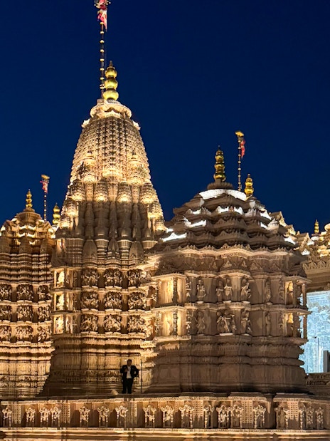 BAPS Hindu Temple illuminated at night, intricate carvings visible, Dubai tour.
