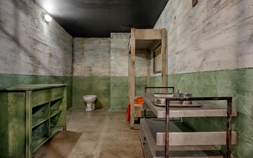 Escape room interior with bunk bed, metal table, and toilet at Neverland Bar & Escape Room.