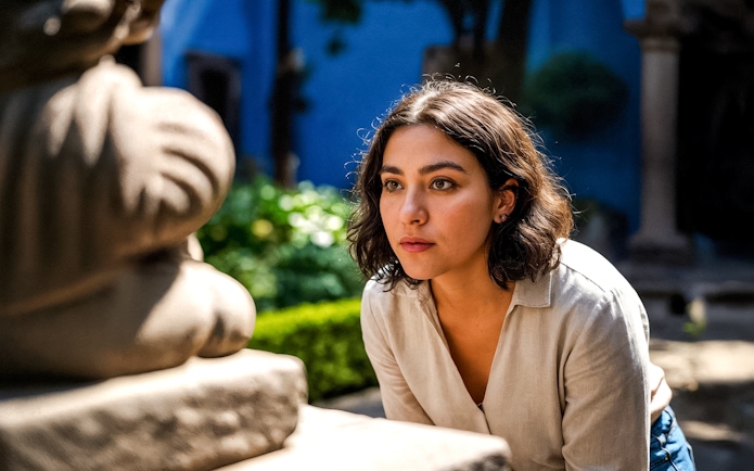 Tourist observing sculpture in Frida Kahlo Museum courtyard, Mexico City.