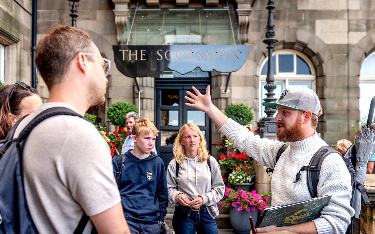Tour guide leading a Harry Potter-themed tour in Edinburgh, speaking to tourists outside The Scotsman.