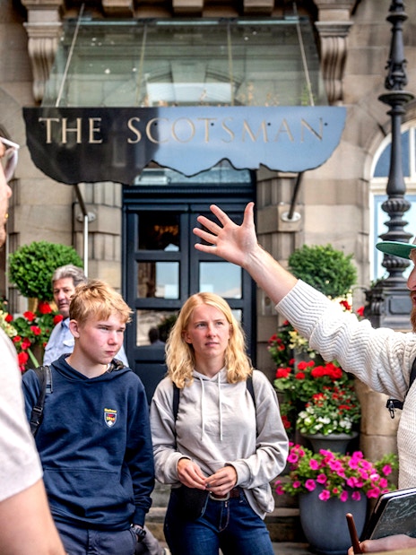 Tour guide leading a Harry Potter-themed tour in Edinburgh, speaking to tourists outside The Scotsman.