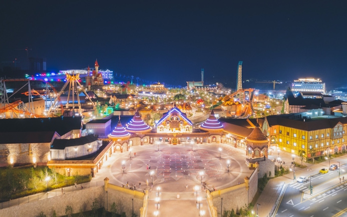 Nighttime aerial view of Lotte World Adventure Busan, featuring illuminated rides and attractions.