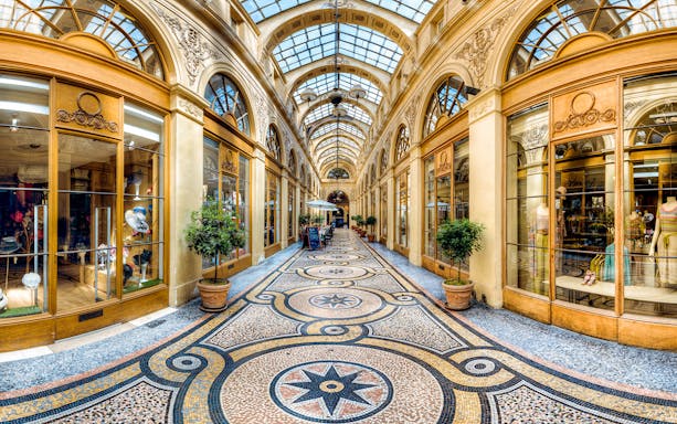Covered passage in Paris with ornate glass ceiling and boutique shops.