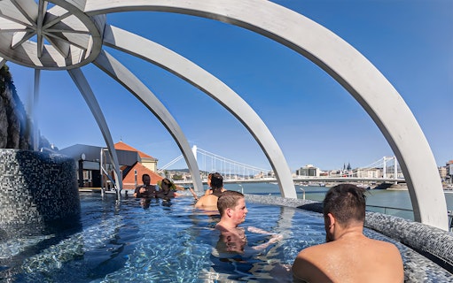 Visitors relaxing in the rooftop pool at Rudas Thermal Spa, Budapest, with city views.