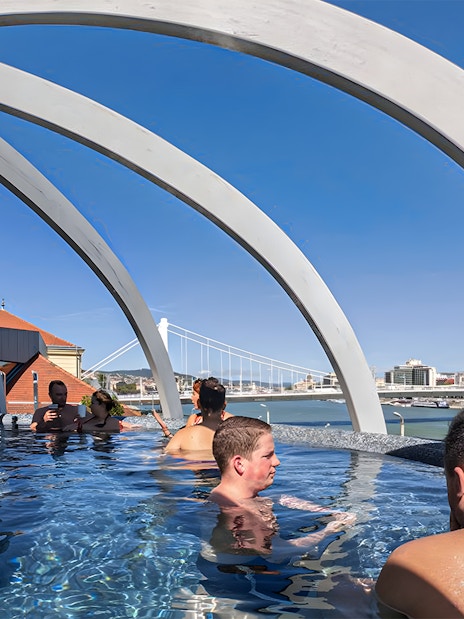 Visitors relaxing in the rooftop pool at Rudas Thermal Spa, Budapest, with city views.