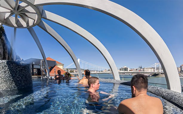Visitors relaxing in the rooftop pool at Rudas Thermal Spa, Budapest, with city views.