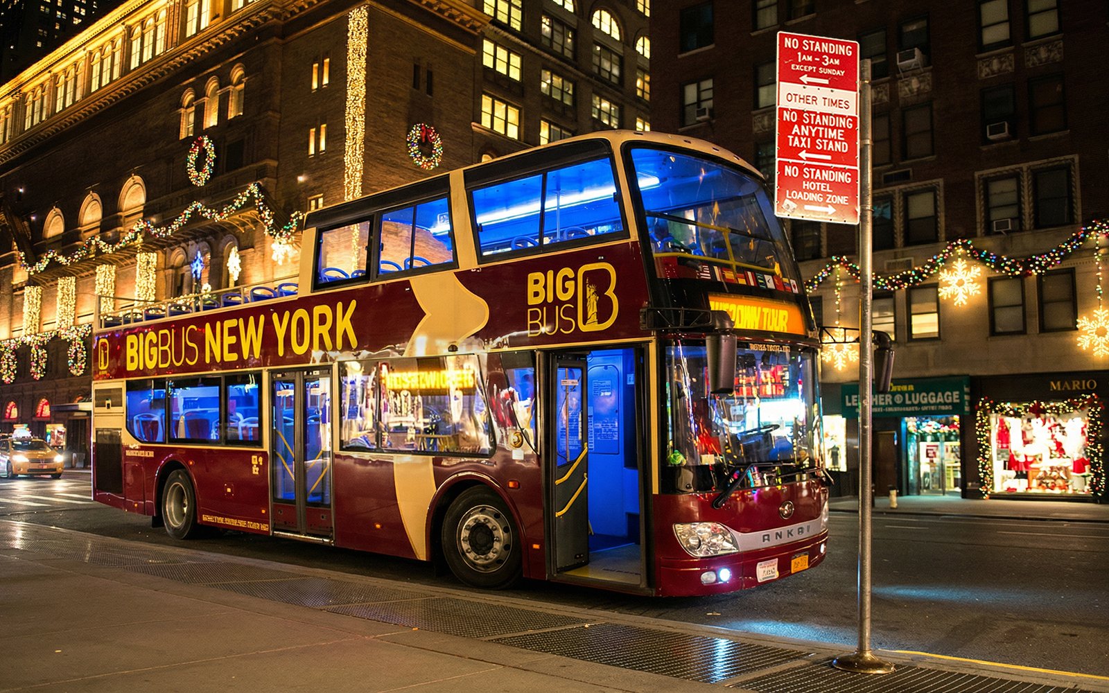 Big Bus New York at night with Christmas lights on city street.