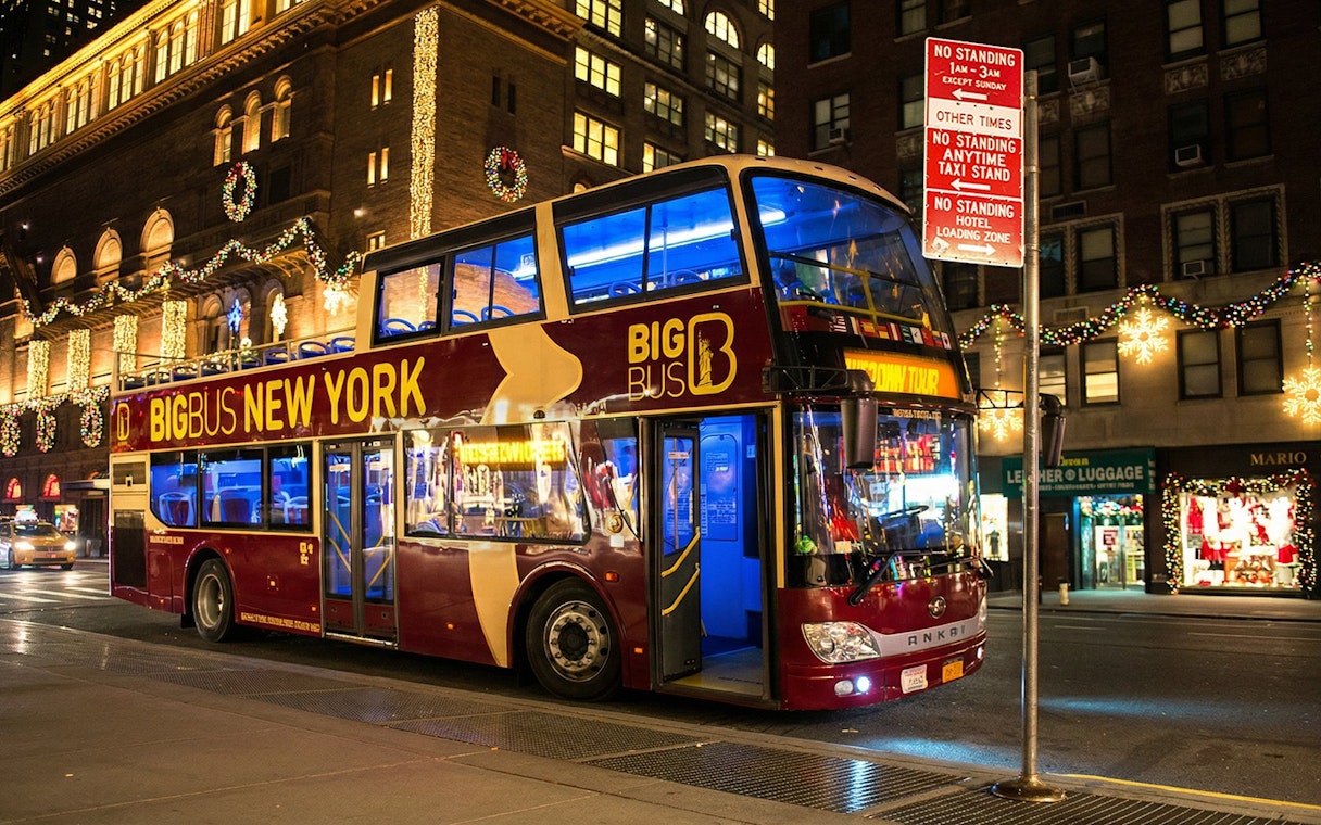 Big Bus New York at night with Christmas lights on city street.