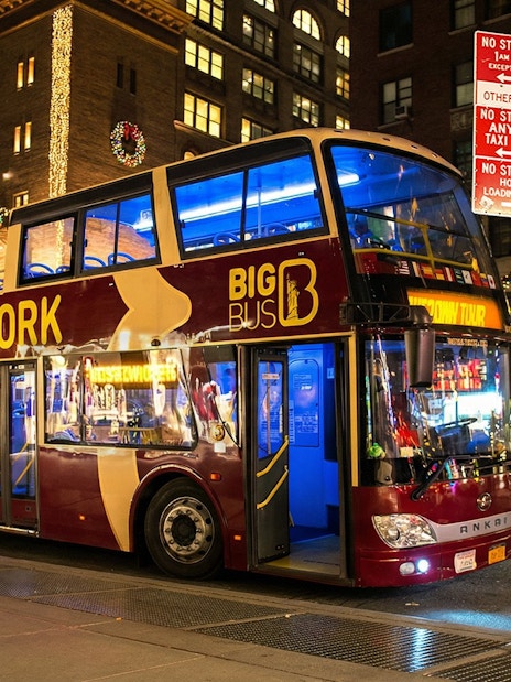 Big Bus New York at night with Christmas lights on city street.