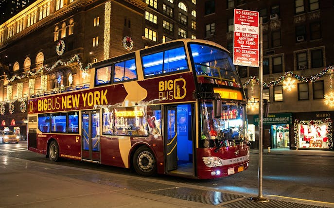Big Bus New York at night with Christmas lights on city street.