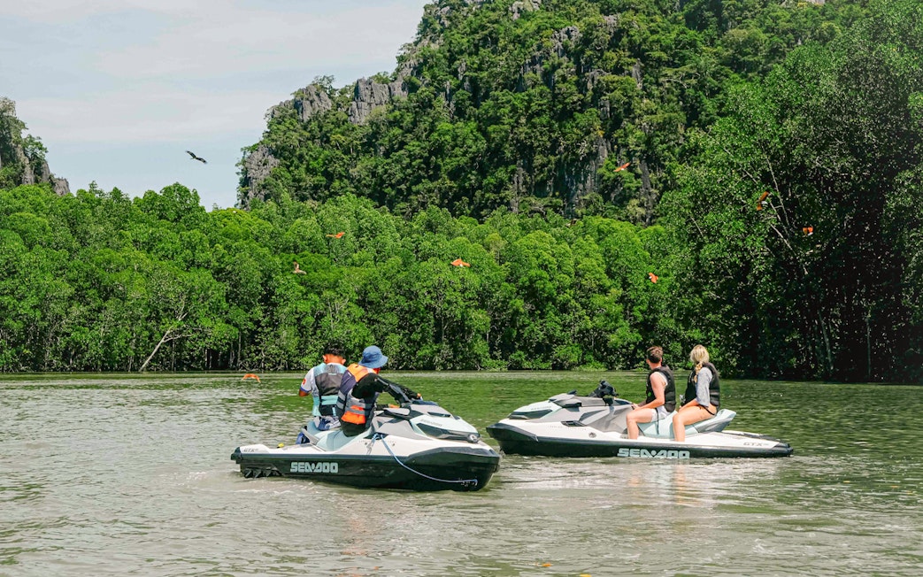 Jet skis on Langkawi's Kilim Geopark waters with lush greenery and limestone cliffs.