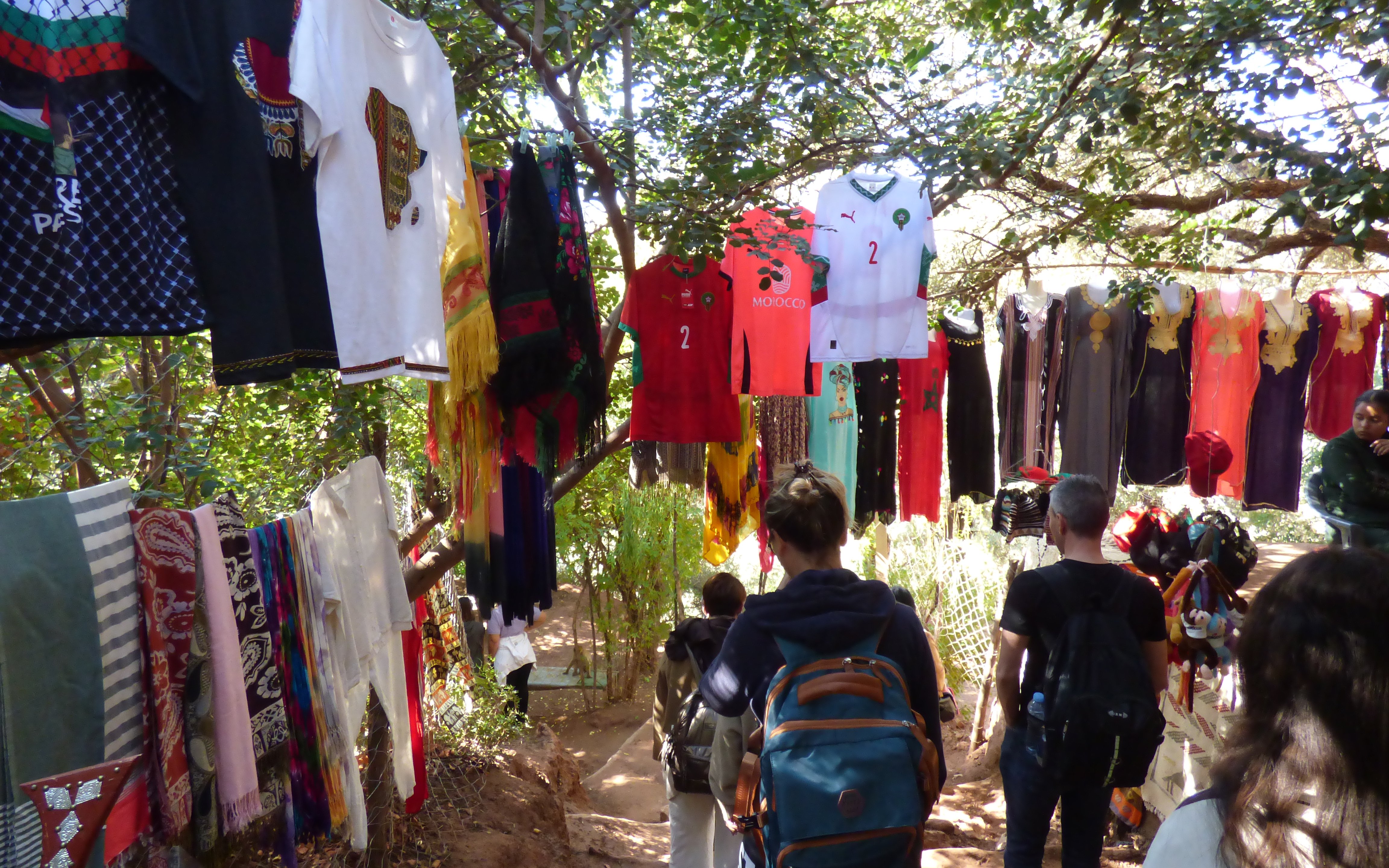 Tourists walking past colorful clothing stalls on the Ouzoud Waterfalls hike in Morocco.