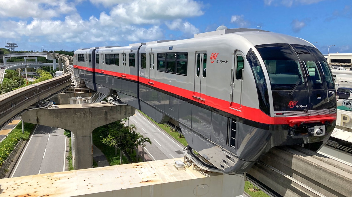 Okinawa Monorail train traveling on elevated tracks under a blue sky.