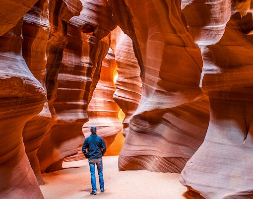 Person exploring narrow sandstone walls in Upper Antelope Canyon, Arizona.