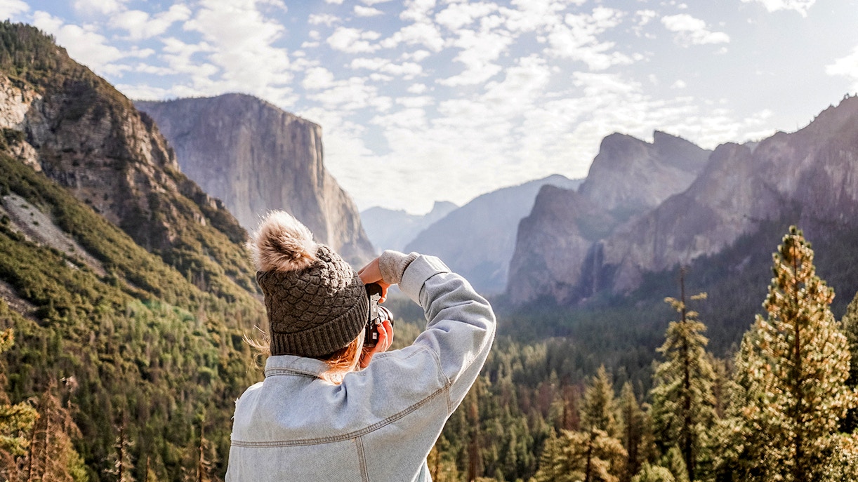 Person photographing Yosemite Valley's cliffs and forest.