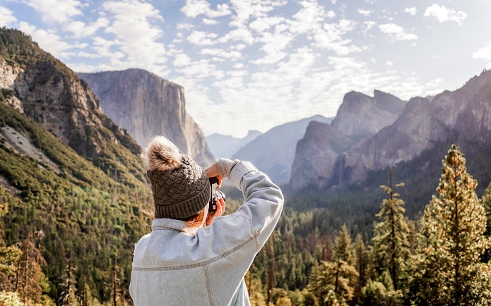 Person photographing Yosemite Valley's cliffs and forest.