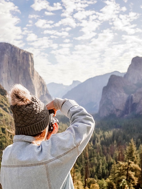 Person photographing Yosemite Valley's cliffs and forest.