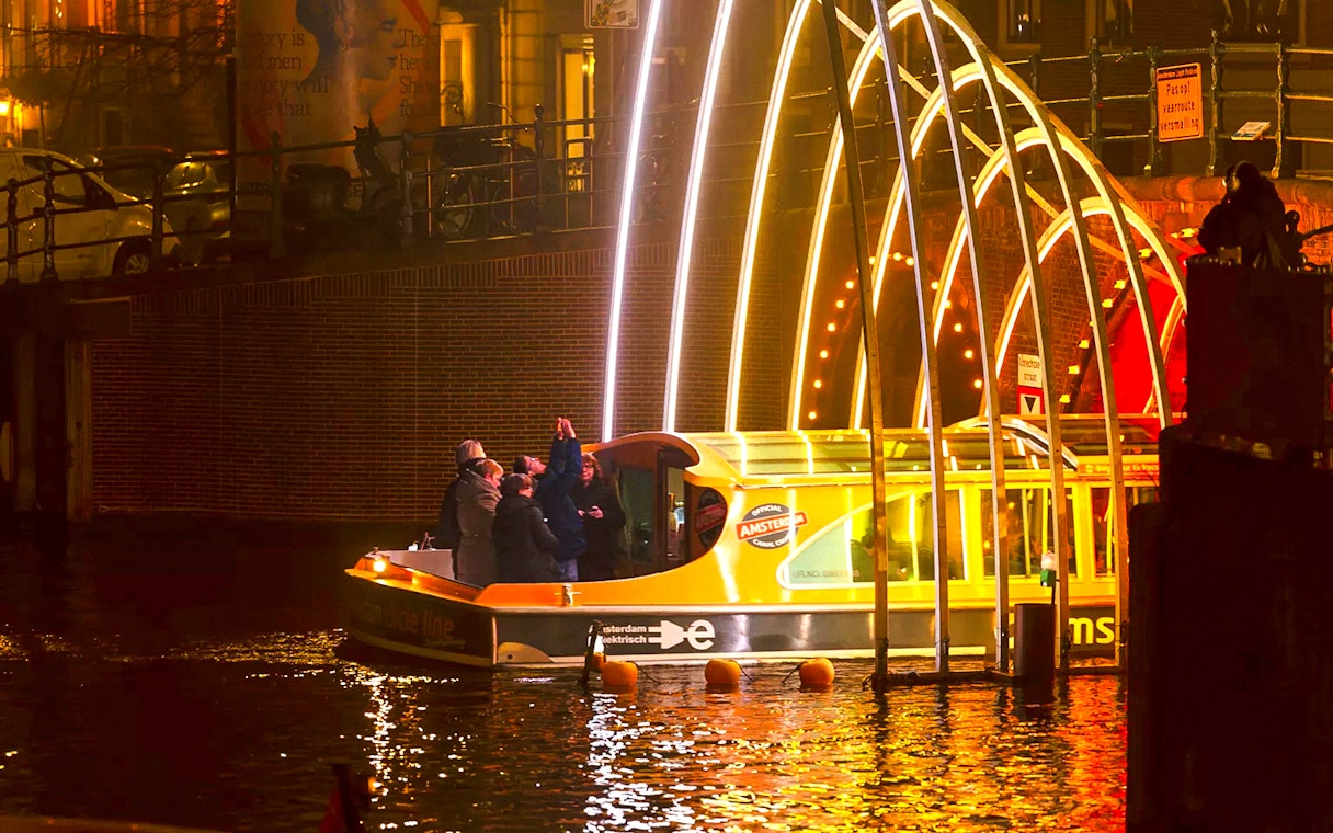 Amsterdam Light Festival cruise boat under illuminated arches at night.