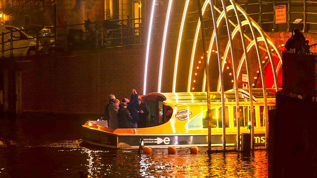 Amsterdam Light Festival cruise boat under illuminated arches at night.