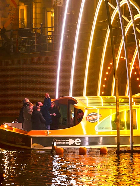 Amsterdam Light Festival cruise boat under illuminated arches at night.