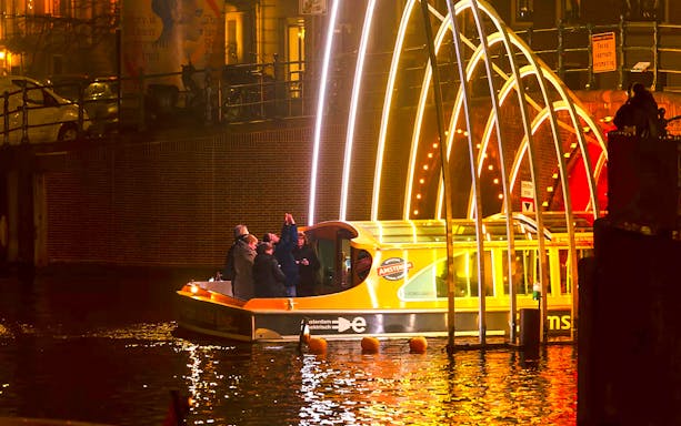 Amsterdam Light Festival cruise boat under illuminated arches at night.