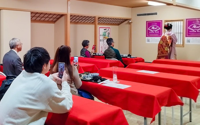 Guests watching a Maiko dance performance during a tea ceremony in a traditional Japanese setting.