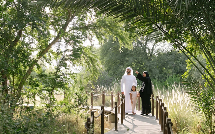 Family exploring lush greenery on Al Noor Island boardwalk.