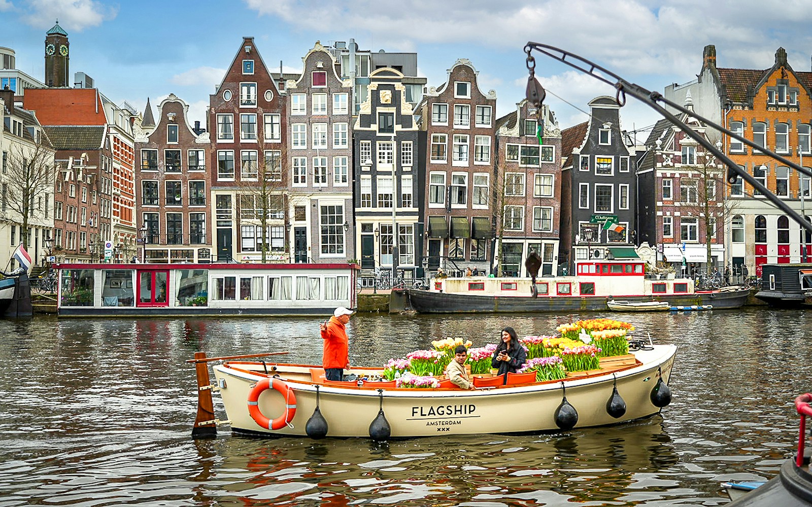 Boat sailing through Amsterdam canal during Tulip Tour with colorful tulip fields in the background.