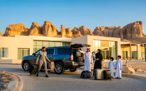 Family with luggage at AlUla private airport transfer, Medina desert backdrop.