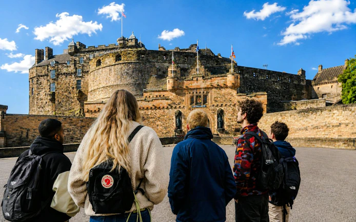 Tour group outside Edinburgh Castle's historic stone architecture in Scotland.