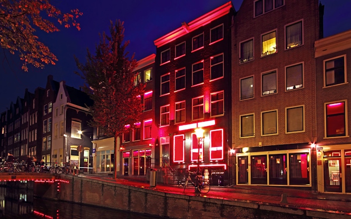 Amsterdam red-light district buildings illuminated at night along a canal.