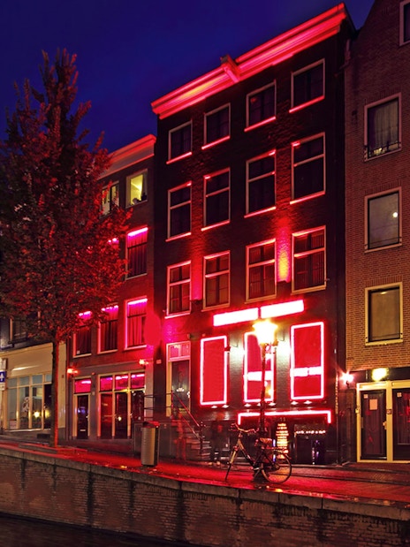 Amsterdam red-light district buildings illuminated at night along a canal.