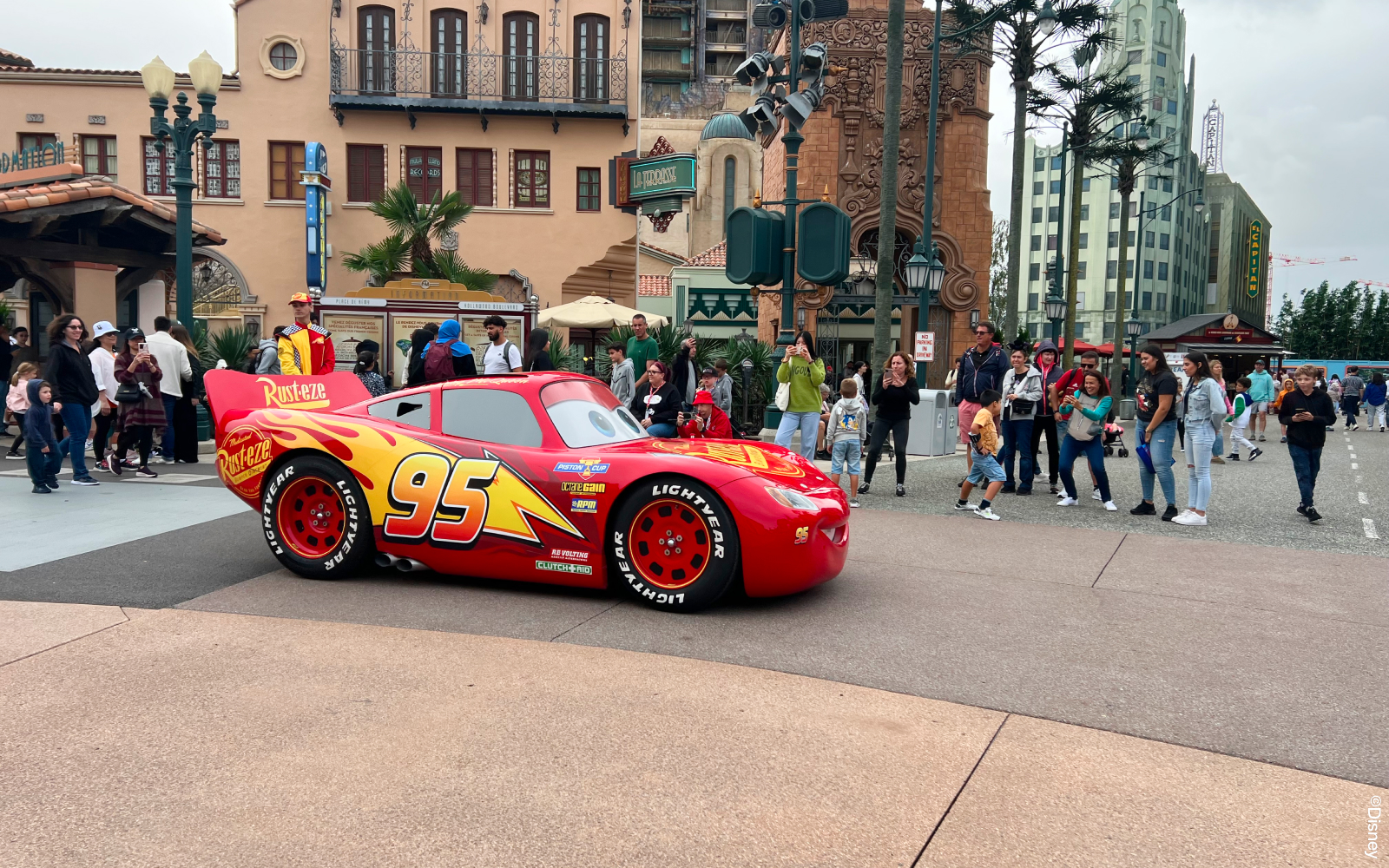 Red race car with number 95 at Disneyland Paris, surrounded by visitors.