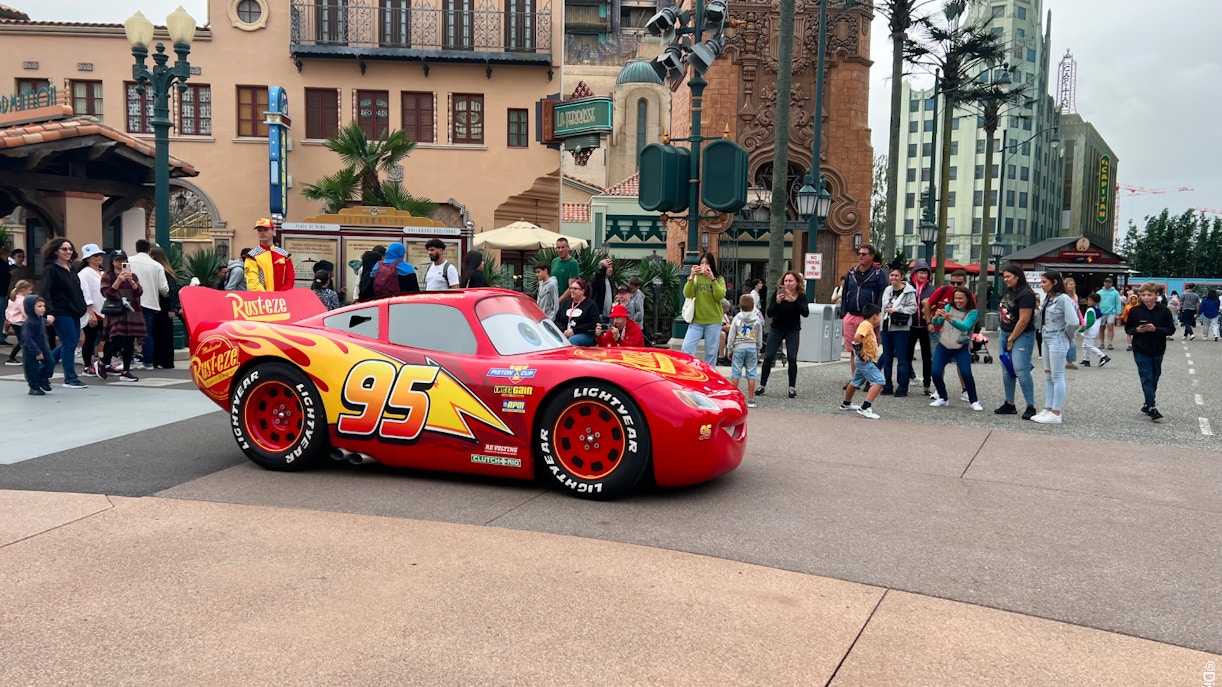 Red race car with number 95 at Disneyland Paris, surrounded by visitors.