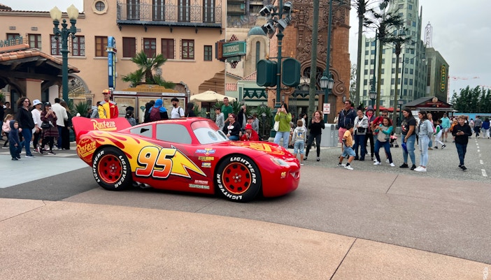 Red race car with number 95 at Disneyland Paris, surrounded by visitors.