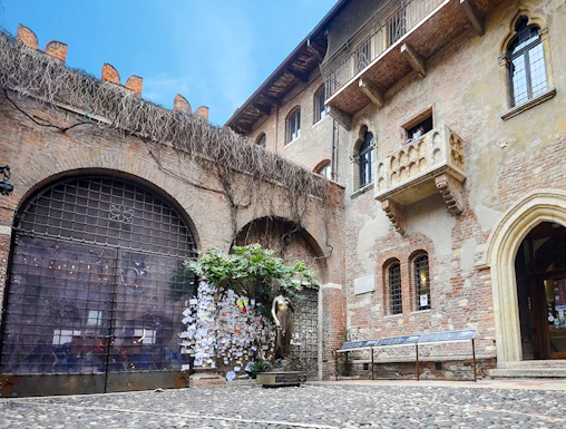 Juliet's balcony at Casa di Giulietta, Verona, with tourists in the courtyard.