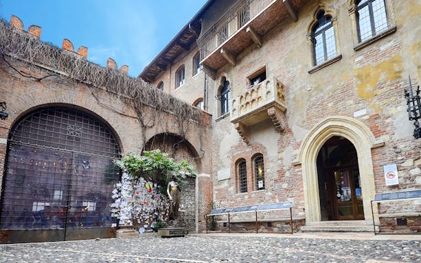 Juliet's balcony at Casa di Giulietta, Verona, with tourists in the courtyard.