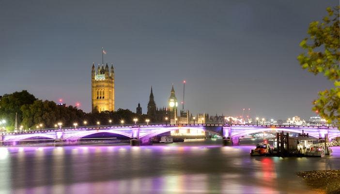 Westminster Bridge and Big Ben illuminated at night on the Thames River, London, UK.