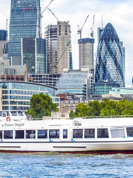 Sightseeing cruise boat on the Thames River with London skyline in the background.