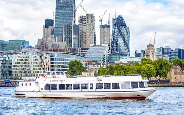 Sightseeing cruise boat on the Thames River with London skyline in the background.