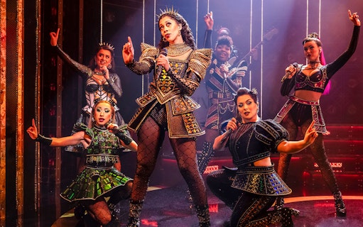 Performers in vibrant costumes on stage during the musical "Six.