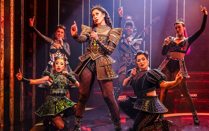 Performers in vibrant costumes on stage during the musical "Six.